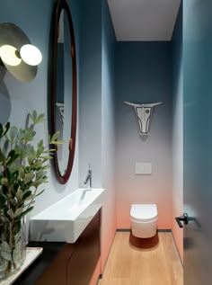 a bathroom with a toilet, sink and mirror on the wall next to a potted plant