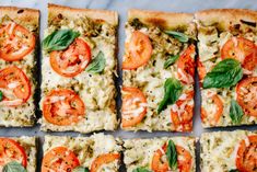 several square slices of pizza with tomatoes and basil on top, cut into eight squares