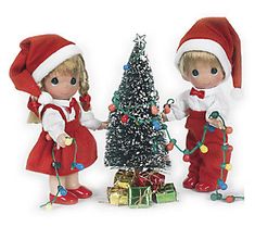 two dolls are standing next to a christmas tree