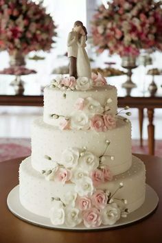 a white wedding cake with pink flowers and a bride and groom figurine on top