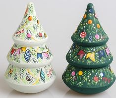 two ceramic christmas trees are sitting next to each other on a white surface, one is painted green and the other is decorated with colorful ornaments