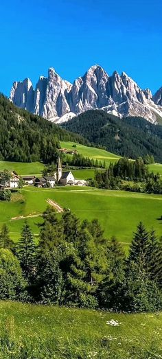 the mountains are covered in snow and green grass, while houses stand on either side