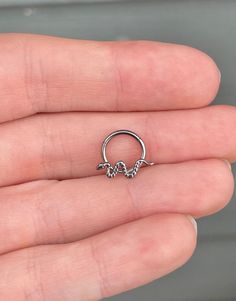 a person is holding a small silver nose ring in their left hand and there are two tiny beads hanging from the end of it