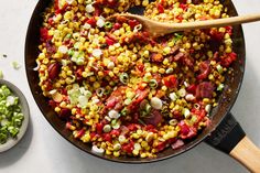 a skillet filled with corn and vegetables next to a wooden spoon