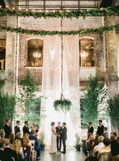 a couple getting married in front of an indoor wedding ceremony with greenery on the walls