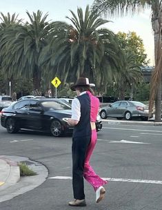 a man in a pink suit and hat crossing the street at an intersection with palm trees