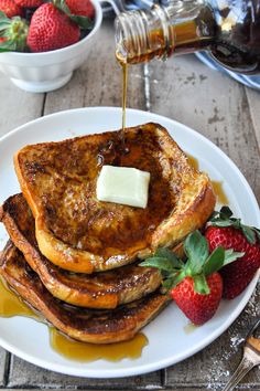 pancakes with syrup and butter on a white plate next to strawberries, honey, and spoons