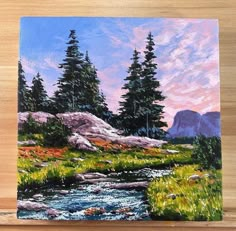 a painting of trees and water on a wooden surface with a mountain in the background