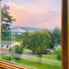 a view out the window of a house with cars parked in the yard and mountains in the distance