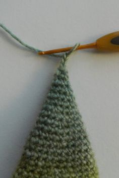 a crocheted triangle with an orange handled knitting needle next to it on a white surface