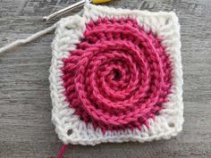 a crochet square with a pink and white flower on it next to a pair of scissors