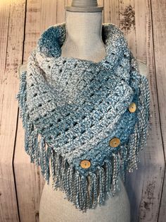 a crocheted scarf with buttons and fringes on a mannequin head