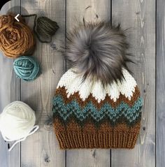 a knitted hat sitting on top of a wooden table next to balls of yarn