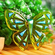 a green butterfly necklace sitting on top of a wooden table next to some planters