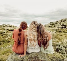 three women sitting on top of a large rock in the middle of an open field