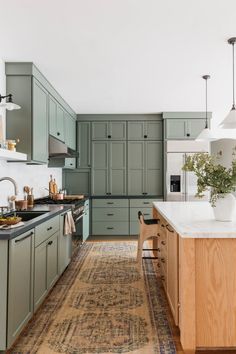 a kitchen with green cabinets and an area rug on the floor in front of it