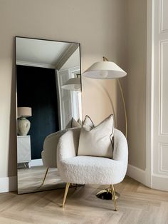 a white chair sitting next to a mirror in a living room under a light fixture