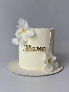 there is a white cake with flowers on it and the word mane spelled in gold