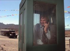 a man talking on a cell phone while standing in front of a green telephone booth