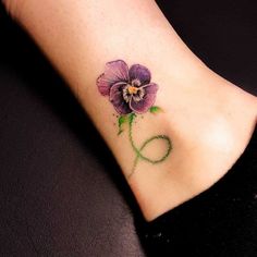 a small purple flower on the ankle with green stems and leaves around it's petals