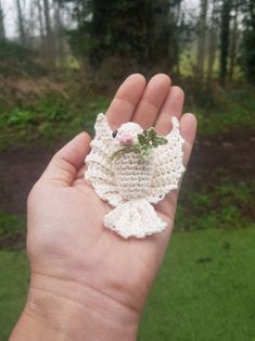 a hand holding a small crocheted bird in it's left palm, with trees in the background