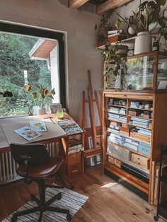 a room with a desk, chair and bookshelf full of books in front of a window