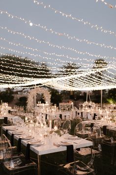 an outdoor wedding reception with clear chairs and string lights strung over the tables at night