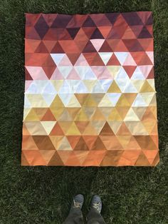 someone is standing in the grass with their feet on a blanket that has triangular shapes