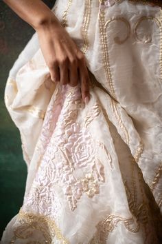 a close up of a person's hand holding onto a white and gold dress