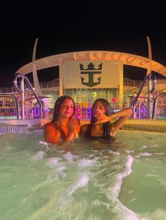 two women are in the pool at night with their arms around each other and smiling