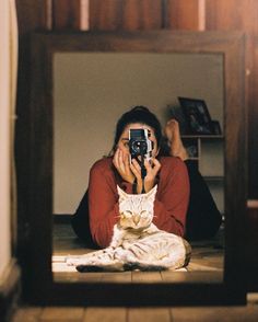 a woman taking a selfie in front of a mirror with a cat on the floor