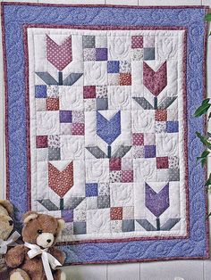 a teddy bear sitting next to a quilted wall hanging on the wall with an arrow design