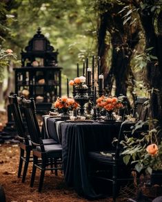 the table is set with black cloths and candles for an elegant dinner in the woods