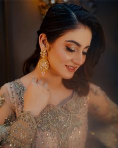 a woman wearing gold earrings and a dress with sequins on the shoulders, standing in front of a mirror