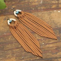 a pair of earrings with long tassels on top of a wooden table next to a plant