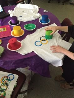 a young boy sitting at a purple table with olympic rings on it and other items around him