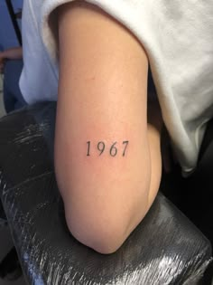 a woman with a small tattoo on her arm that reads,'1917'in cursive font