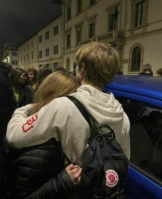 two people hugging each other in front of a blue car