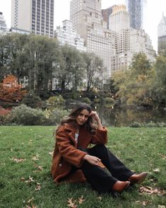 a woman sitting on the grass in front of a cityscape with skyscrapers