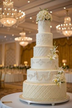 a wedding cake with white flowers on top and chandeliers in the back ground