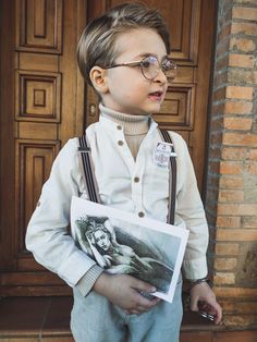 a young boy wearing glasses and suspenders is holding a photo in front of a door