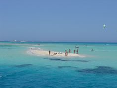 people are standing on the beach and flying kites in the blue water near an island