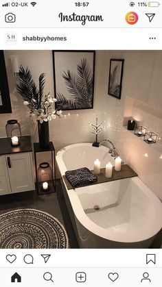 a white bath tub sitting in a bathroom next to two candles and pictures on the wall