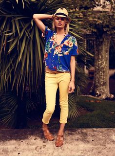 a woman standing in front of a palm tree wearing yellow pants and a blue shirt