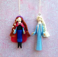 two handmade dolls hanging from strings on a pink and blue wallpapered background