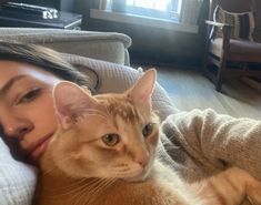 a woman laying on top of a couch next to a large orange and white cat