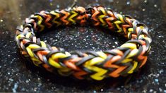 an orange, yellow and black braided bracelet sitting on top of a marble counter