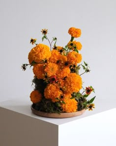 an arrangement of orange flowers on top of a white pedestal in front of a wall