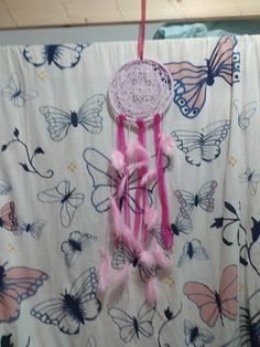 a pink and white crochet dream catcher hanging from a curtain with butterflies on it