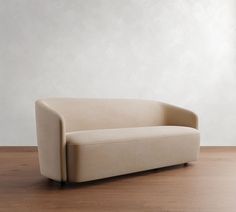 a beige couch sitting on top of a wooden floor next to a white wall in an empty room